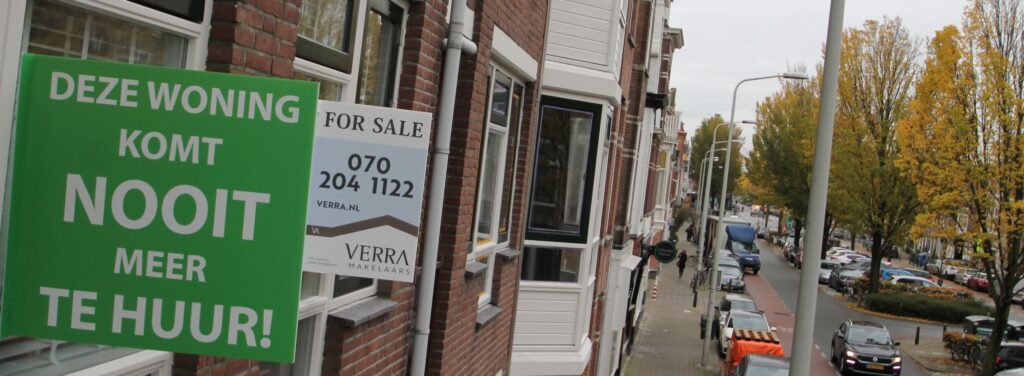 A green real estate sign on an apartment window reading 'Deze woning komt nooit meer te huur' (This property will never be for rent again) next to a standard 'Te Koop' (For Sale) sign, illustrating the Dutch landlord sell-off.