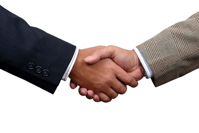 Two people shaking hands over a wooden table, symbolizing a professional agreement between real estate agents and clients.